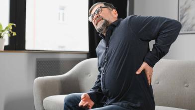 Latino man grimacing in pain and hold his hand on his back by his kidney
