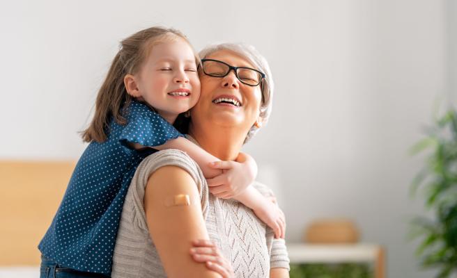 senior woman smiling with a band-aid on her arm and hugging her grandchild