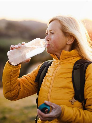 Senior woman walking outdoors drinking from water bottle