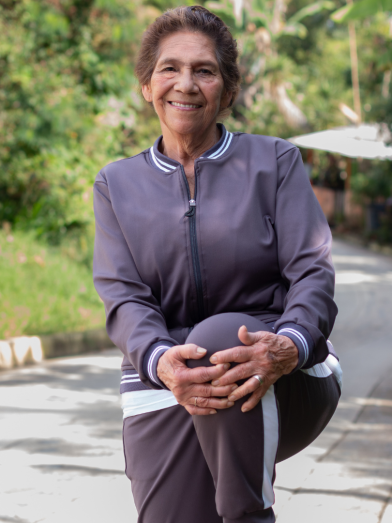 An older woman in a track suit stretches on one leg. 