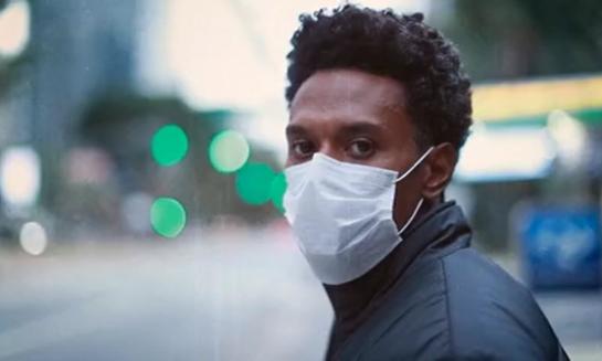 african american man on a city street wearing a mask with a serious look on his face